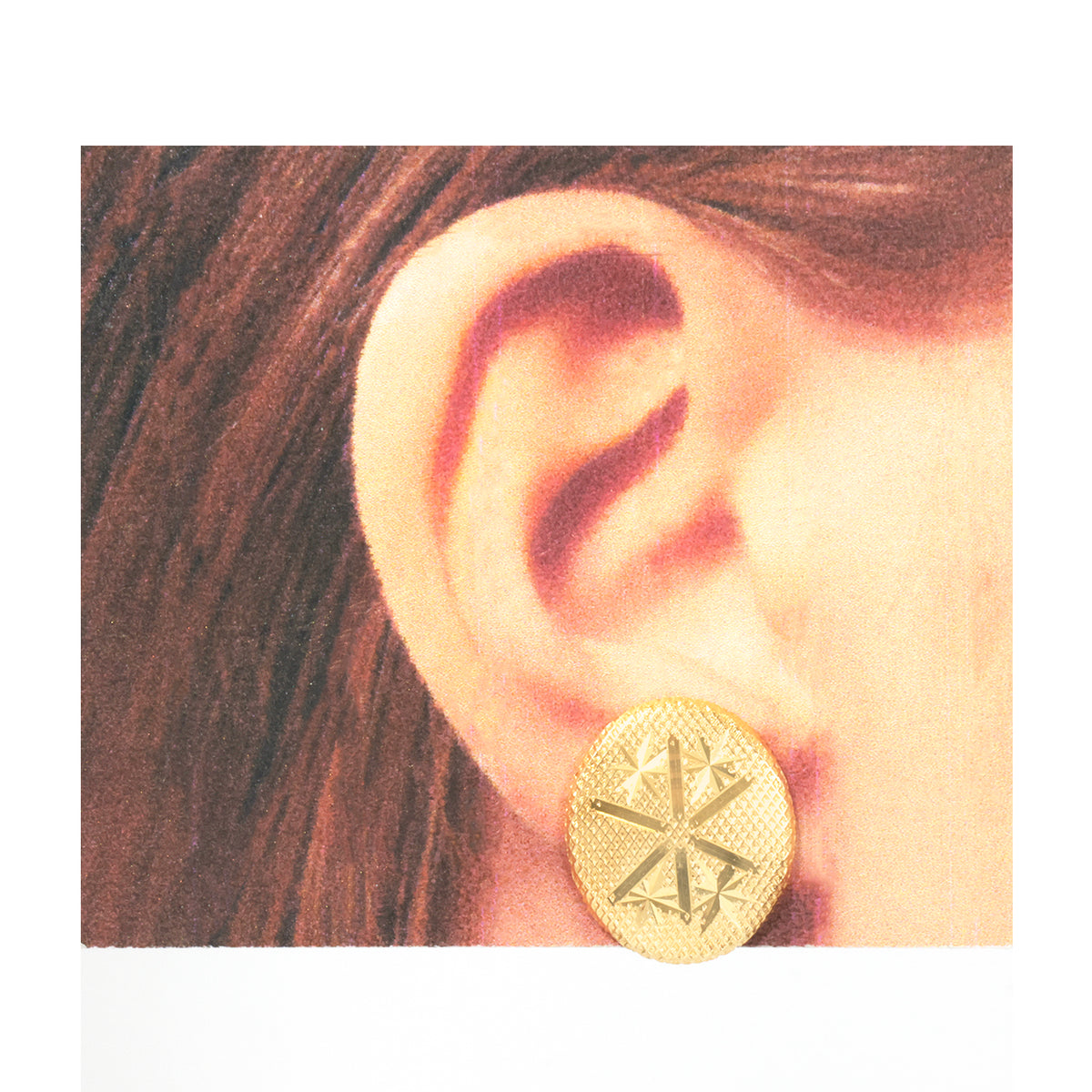 A close-up of a person's ear wearing a round gold stud earring with a textured starburst design.