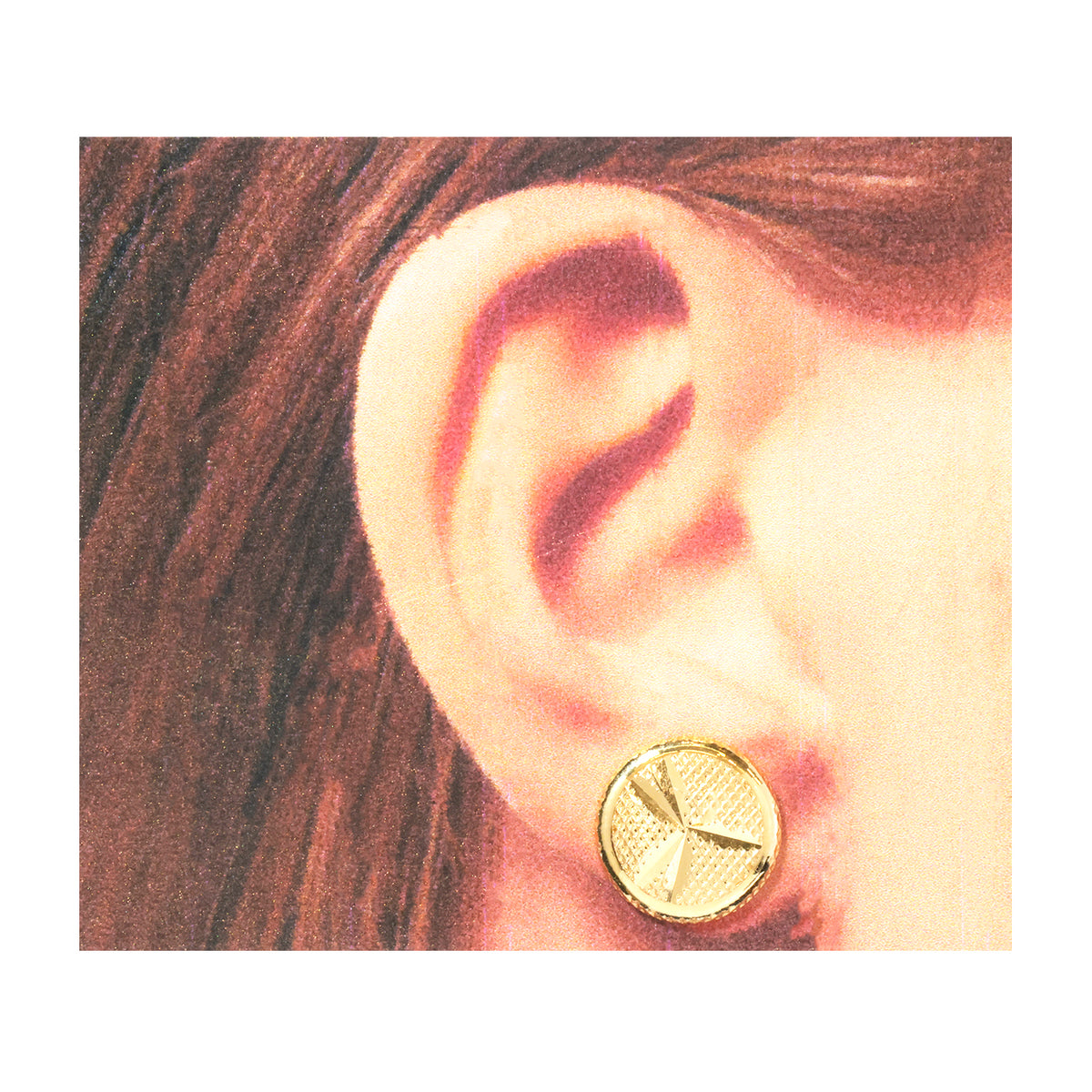 A close-up of a person's ear wearing a small round gold stud earring with a textured geometric design.