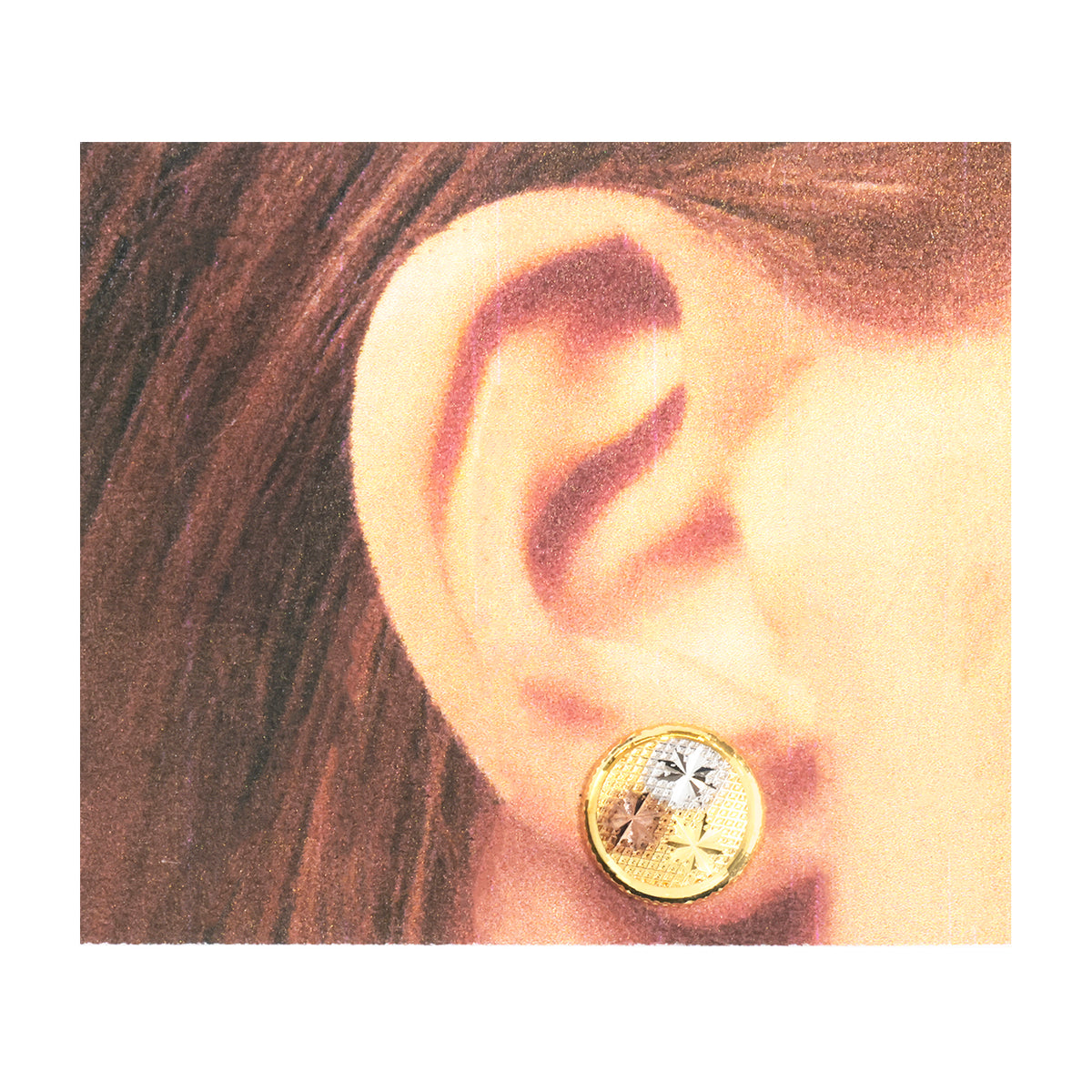 A close-up of a person's ear wearing a round gold-toned stud earring with a small silver-toned floral accent.