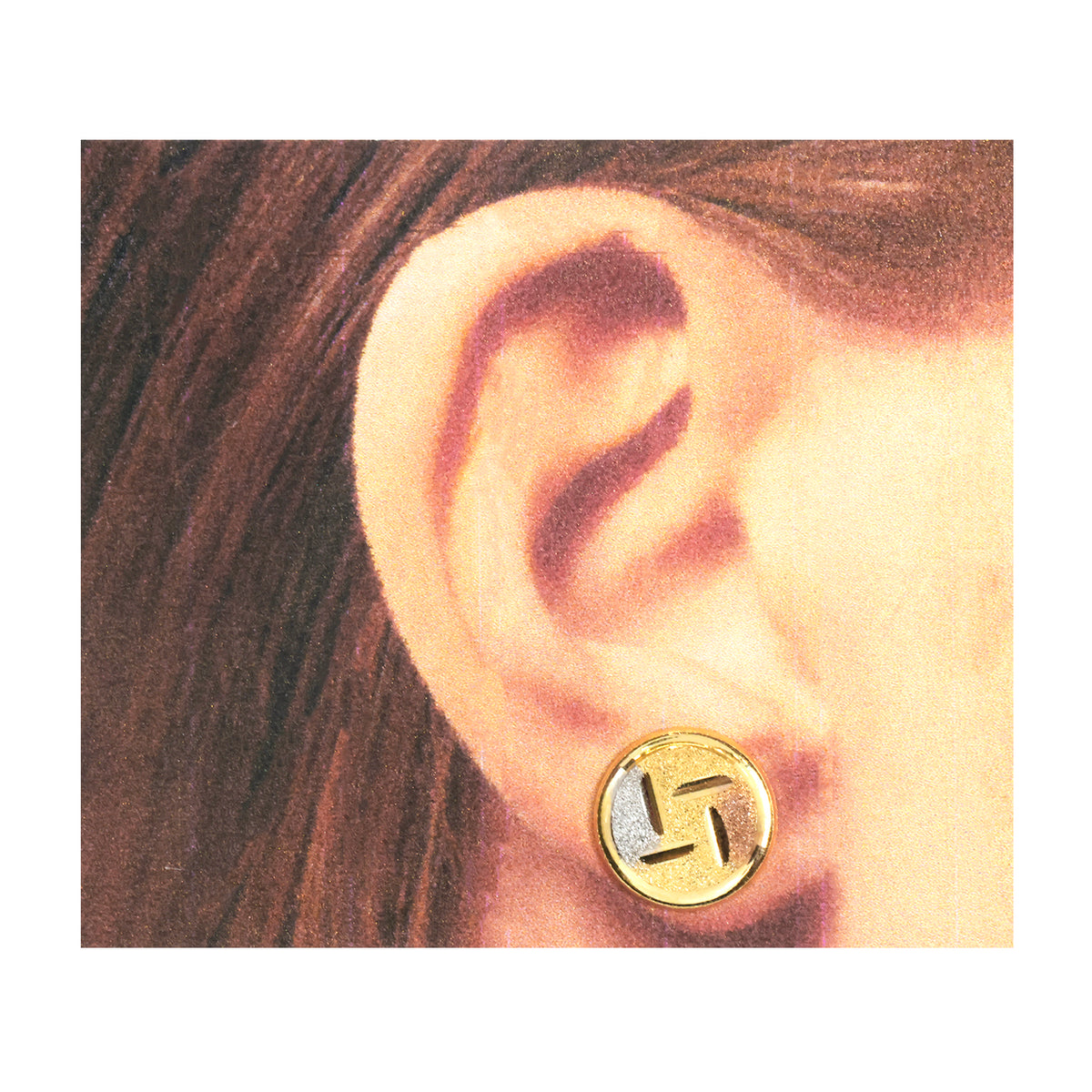 A close-up of a person's ear wearing a round gold stud earring with a silver-toned geometric symbol in the center.