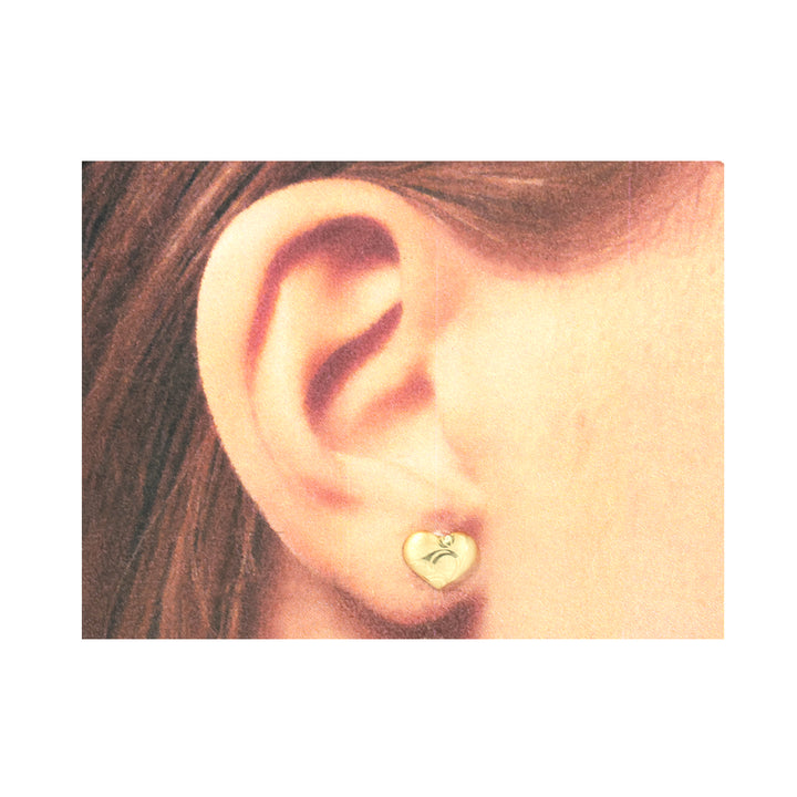 Close-up of an ear wearing a gold heart-shaped earring with a letter 'C' on a white background