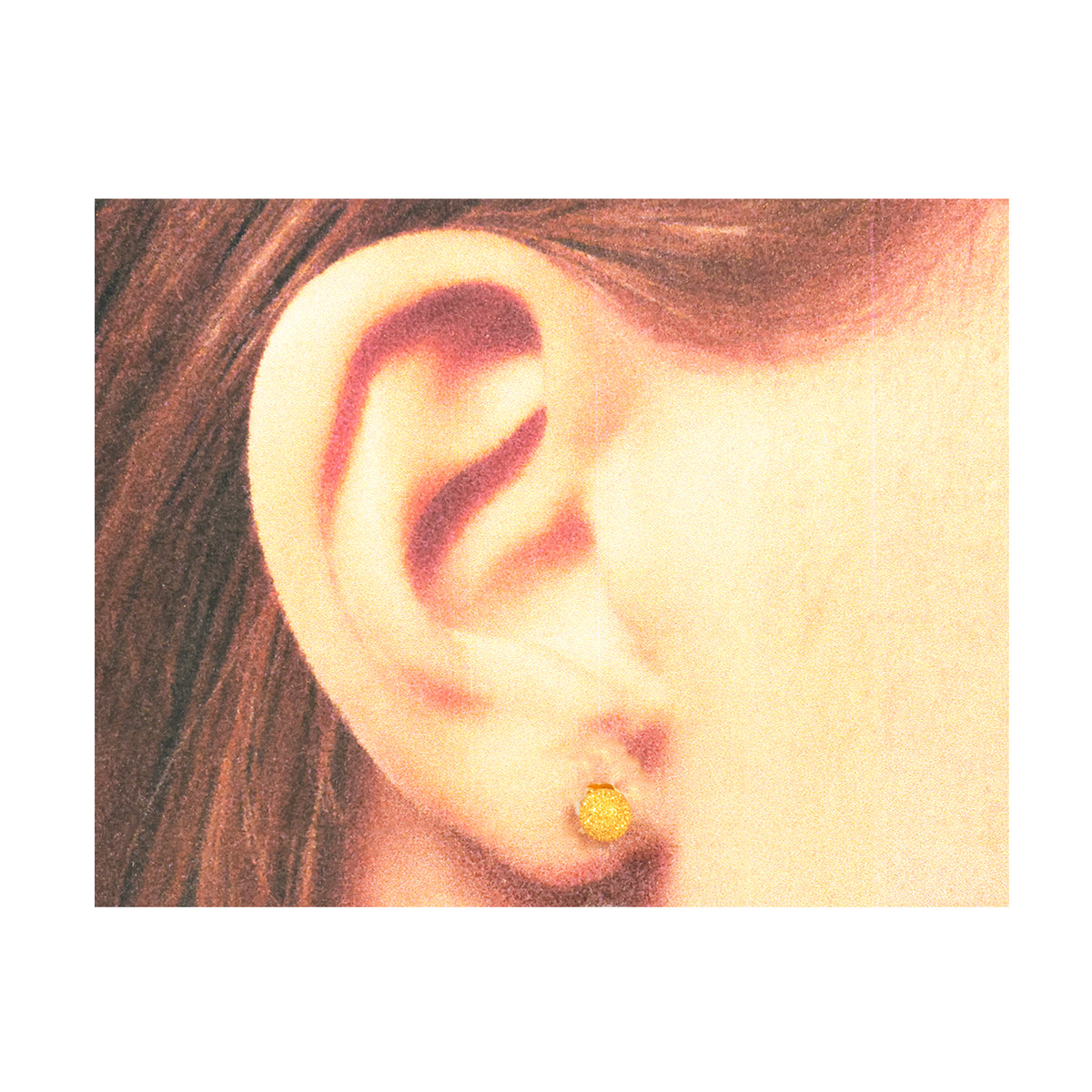 Close-up of an ear wearing a gold earring with hair partially visible.