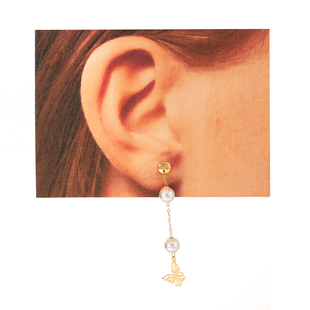Gold and pearl earring worn on an ear with a plain background