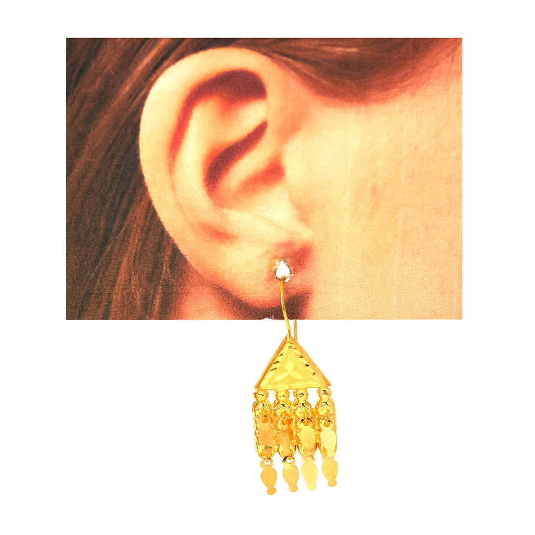 Gold earring worn on an ear with a plain background