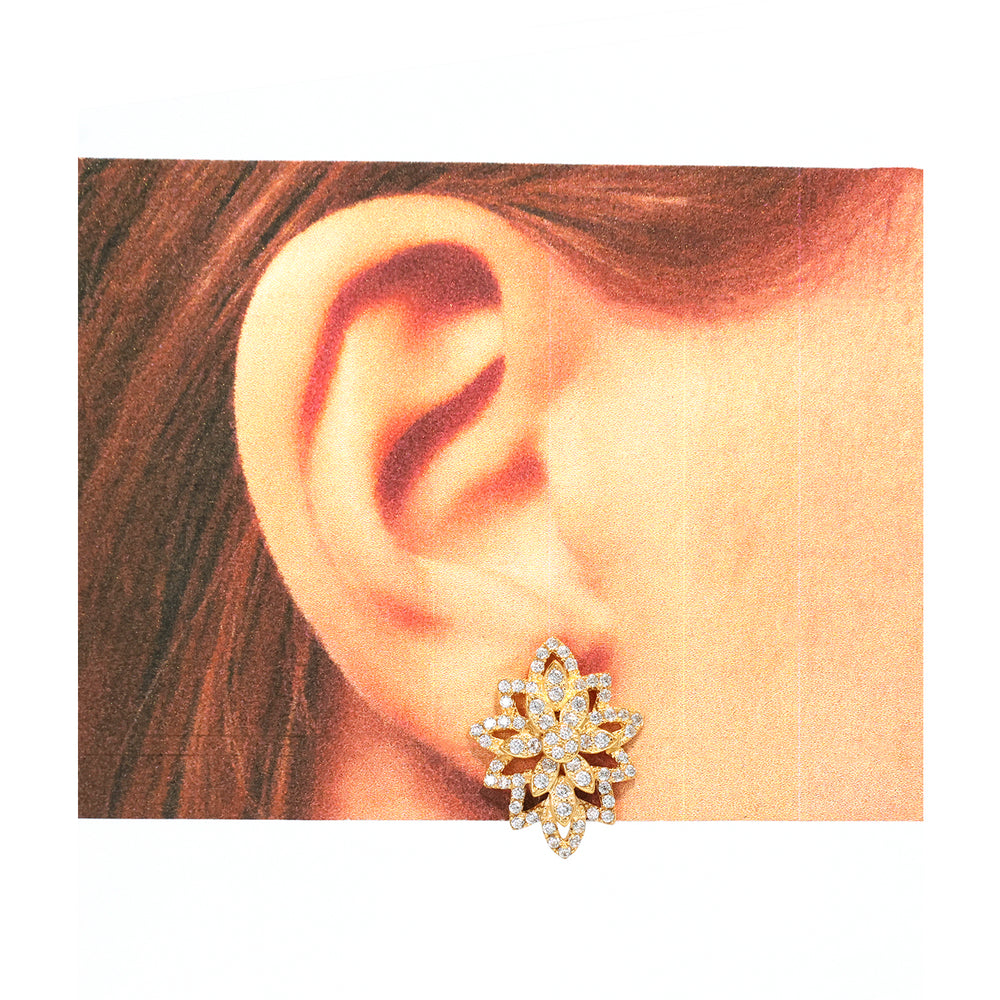 Close-up of an ear wearing a decorative gold earring with a white background