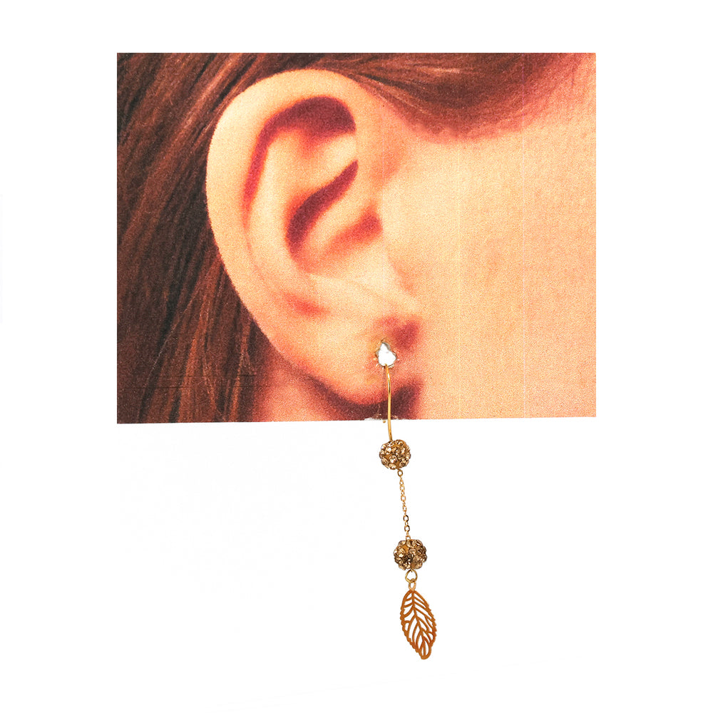 Gold earring with leaf design worn on an ear against a neutral background