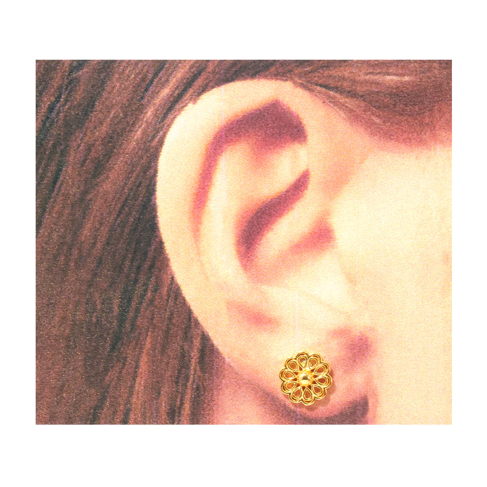 A close-up of a person's ear wearing a small gold stud earring with an intricate floral or sunburst cutout design.