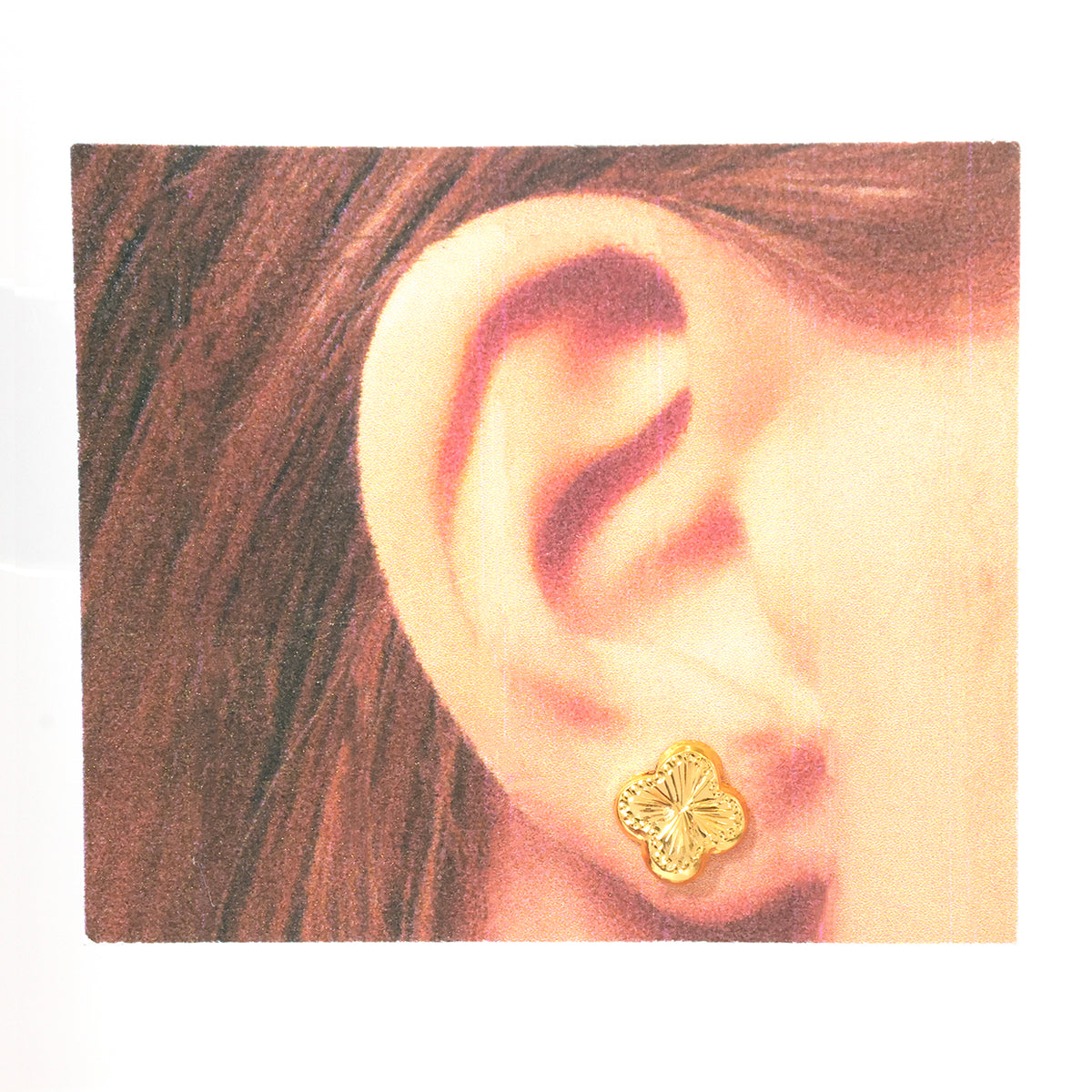 A close-up of a person's ear wearing a small gold stud earring with a textured, organic shape.