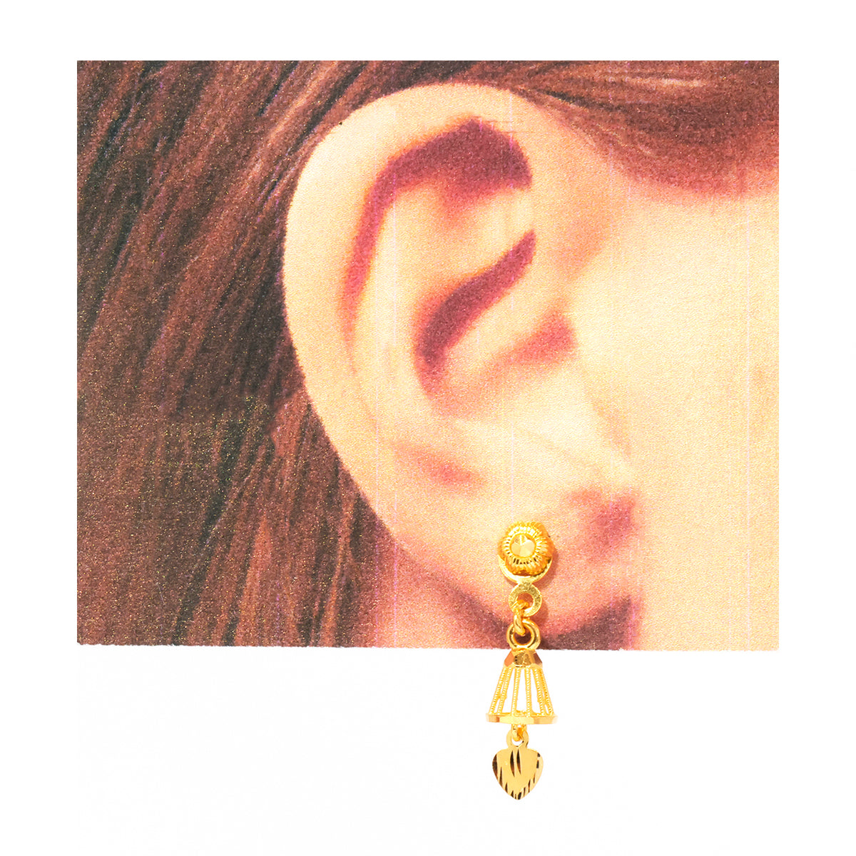 A gold dangle earring with a textured circular top, a small bell-shaped middle section, and a dangling heart-shaped charm, shown worn on a person's ear against a warm-toned background.