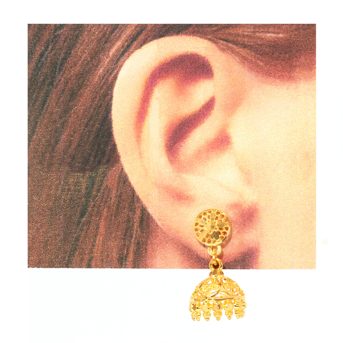 A gold-toned jhumka earring with a circular filigree stud and a dangling bell-shaped charm, shown worn on a person's ear against a white background.