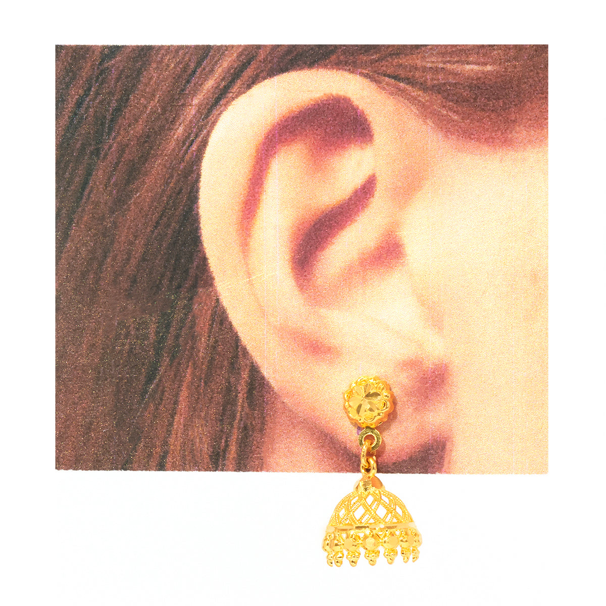A gold-toned jhumka earring with a textured round stud and an openwork bell-shaped dangle, shown worn on a person's ear against a white background.