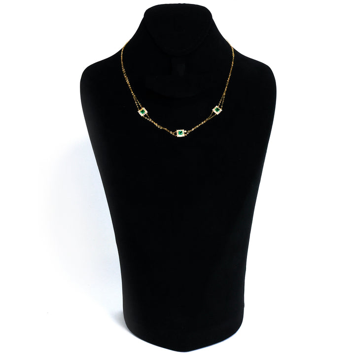 Gold necklace with green gemstones on a black mannequin bust against a white background