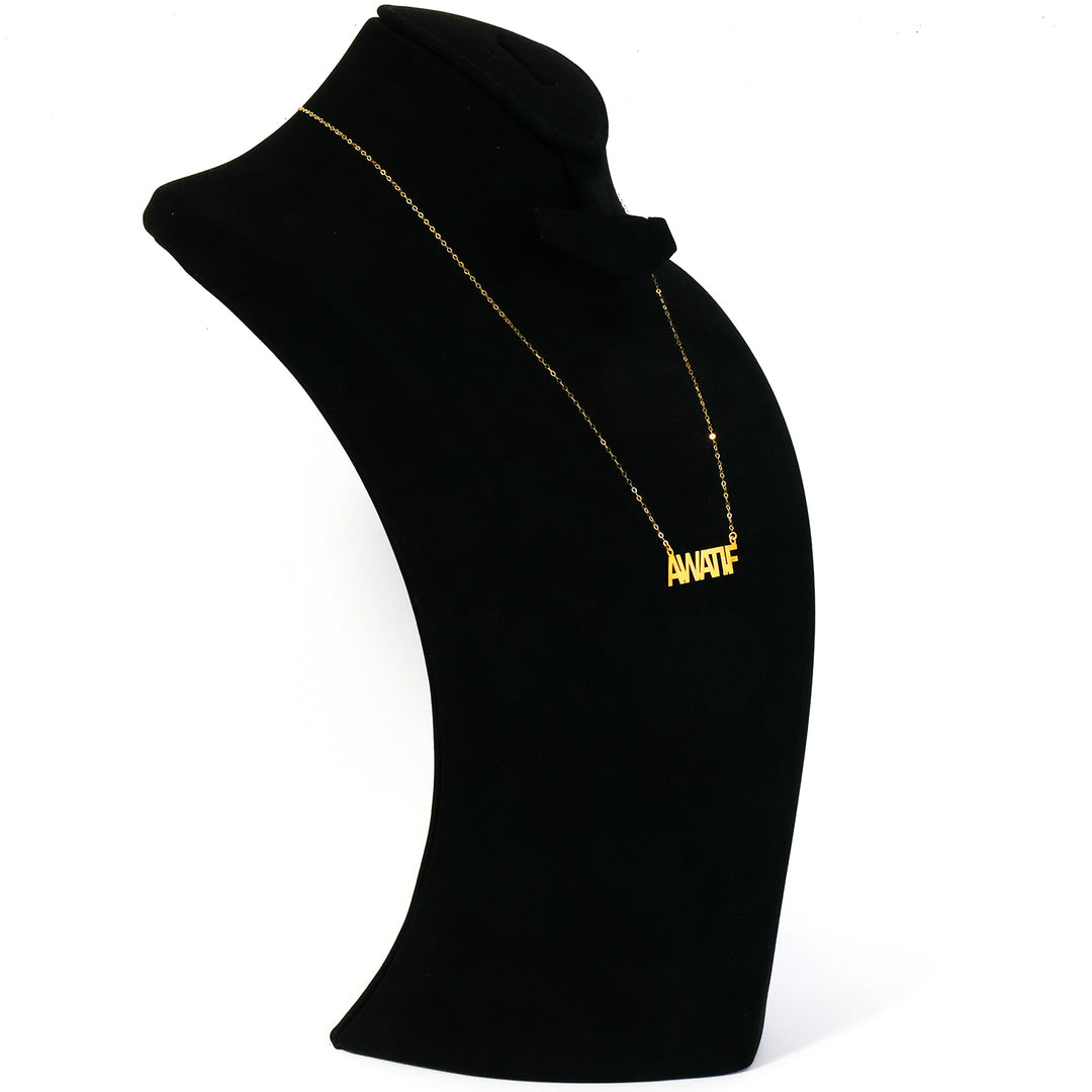 Black turtleneck with gold necklace and 'ANATOL' pendant on a white background