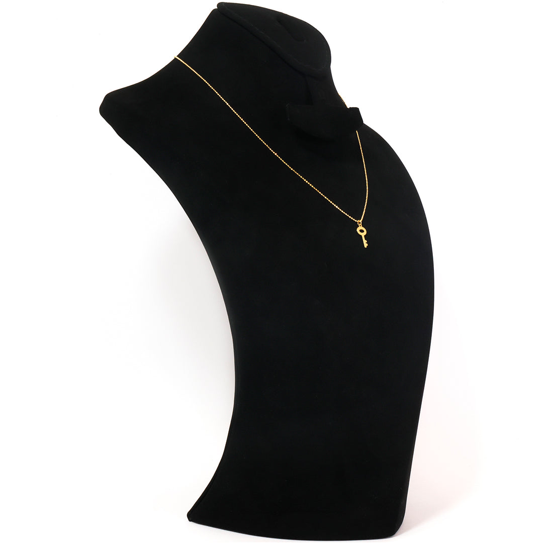 A delicate gold necklace with a small key pendant, displayed on a black velvet jewelry bust against a white background.