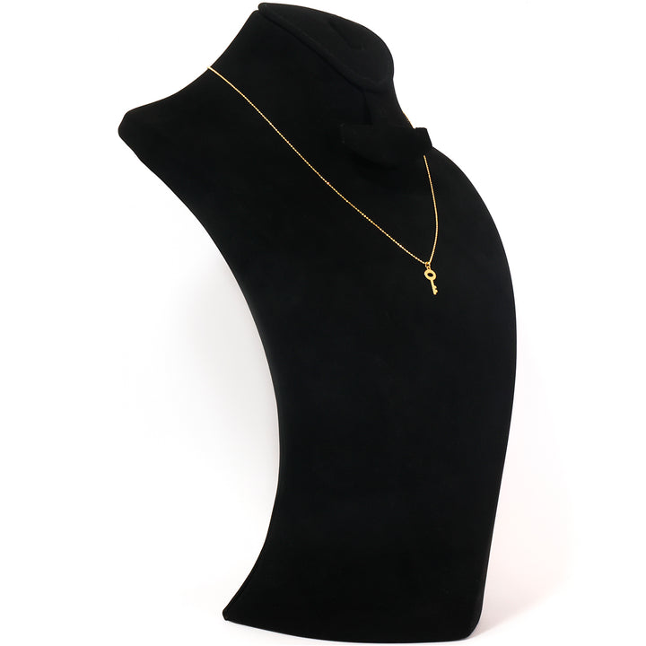 A delicate gold necklace with a small key pendant, displayed on a black velvet jewelry bust against a white background.
