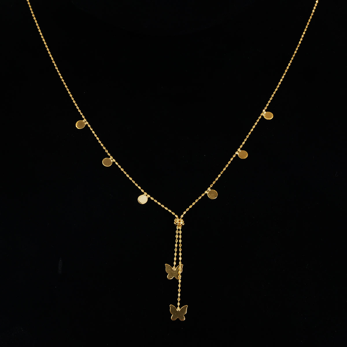 A delicate gold Y-necklace with small flat circular disc charms on the chain and two butterfly pendants hanging from the center, displayed on a black background.