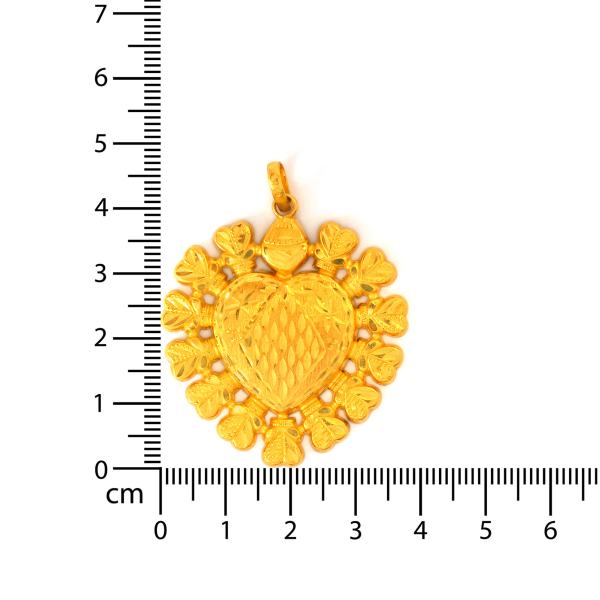 Gold heart-shaped pendant with floral designs on a white background with a ruler for scale.