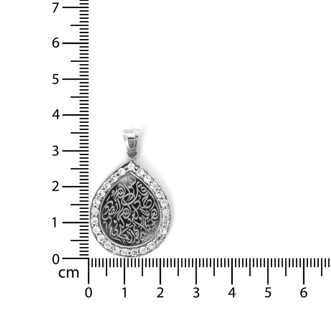 Silver pendant with intricate design on a white background with a ruler for scale.