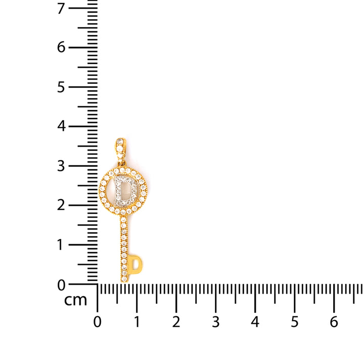 Gold key-shaped pendant with a central stone and smaller stones on a white background with a ruler for scale.