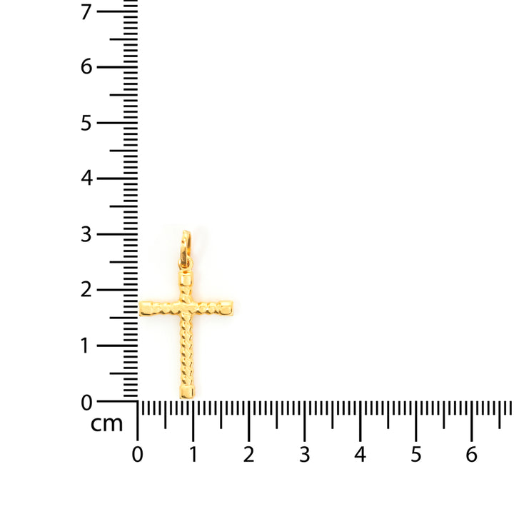 Gold cross pendant next to a ruler on a white background