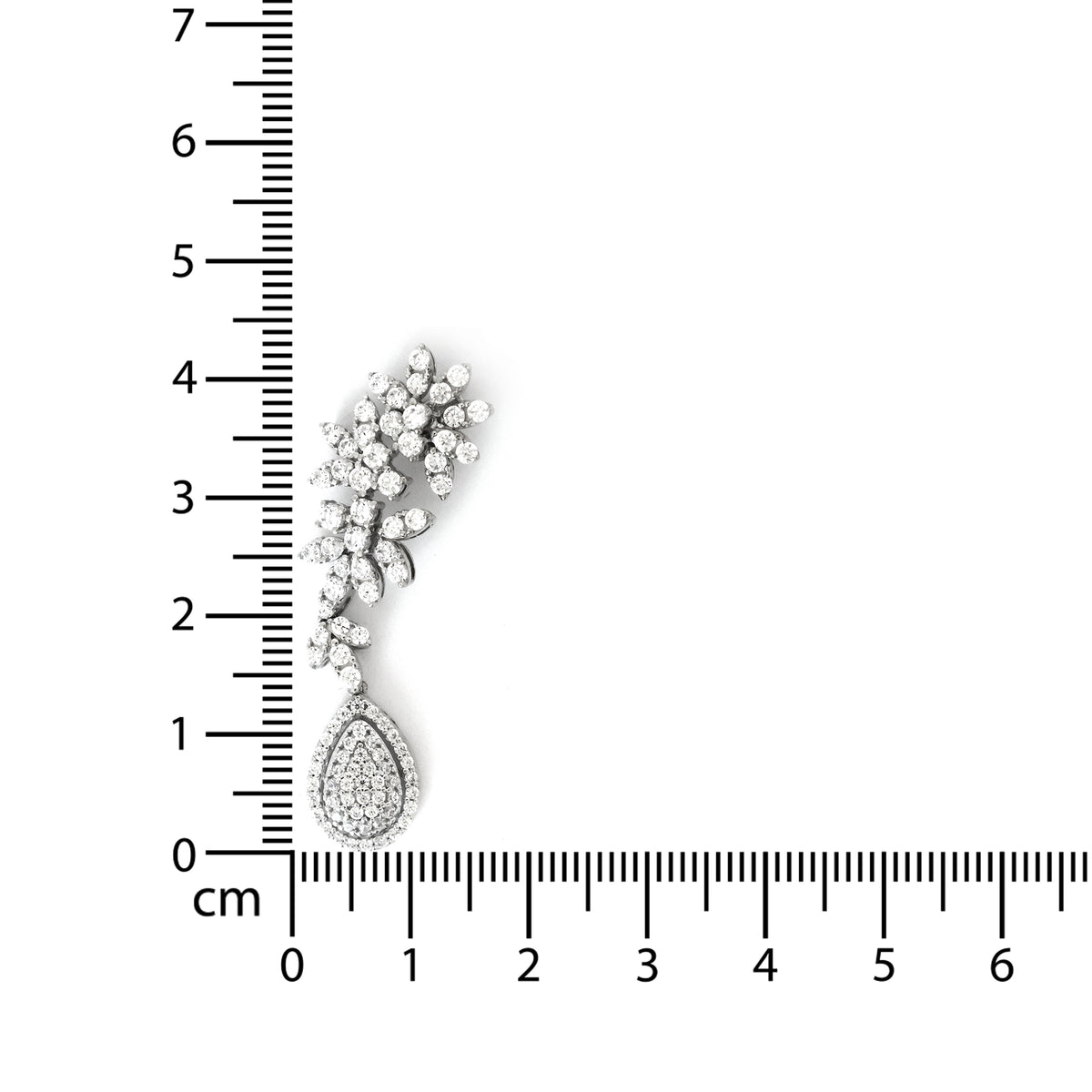 Silver teardrop earring with floral design next to a ruler for scale on a white background