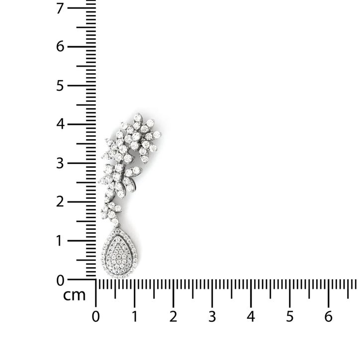 Silver teardrop earring with floral design next to a ruler for scale on a white background