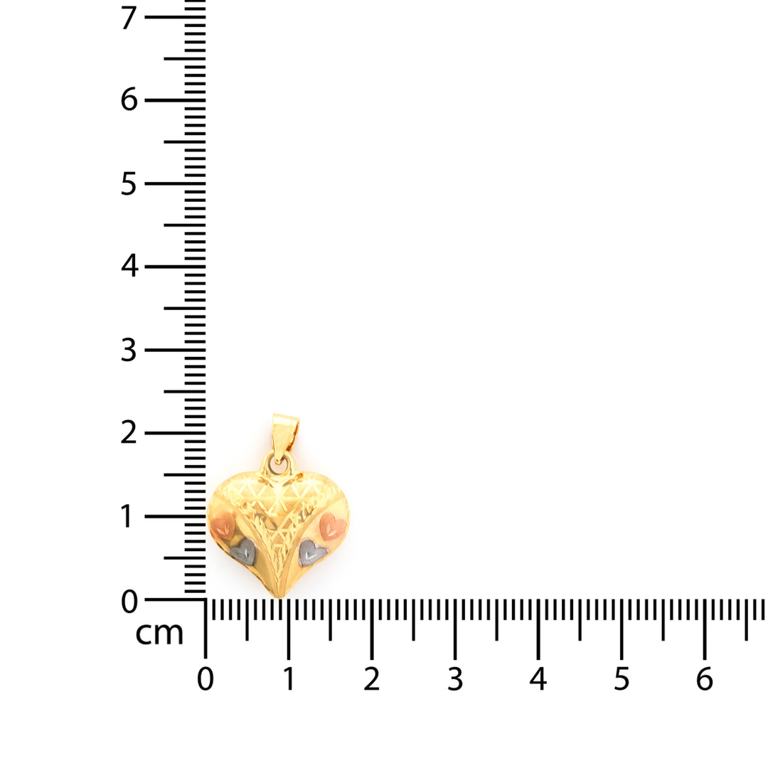 Gold heart-shaped pendant with engraved design on a ruler for scale.