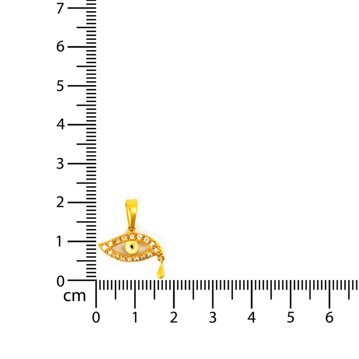 Gold pendant with eye design next to a ruler on a white background
