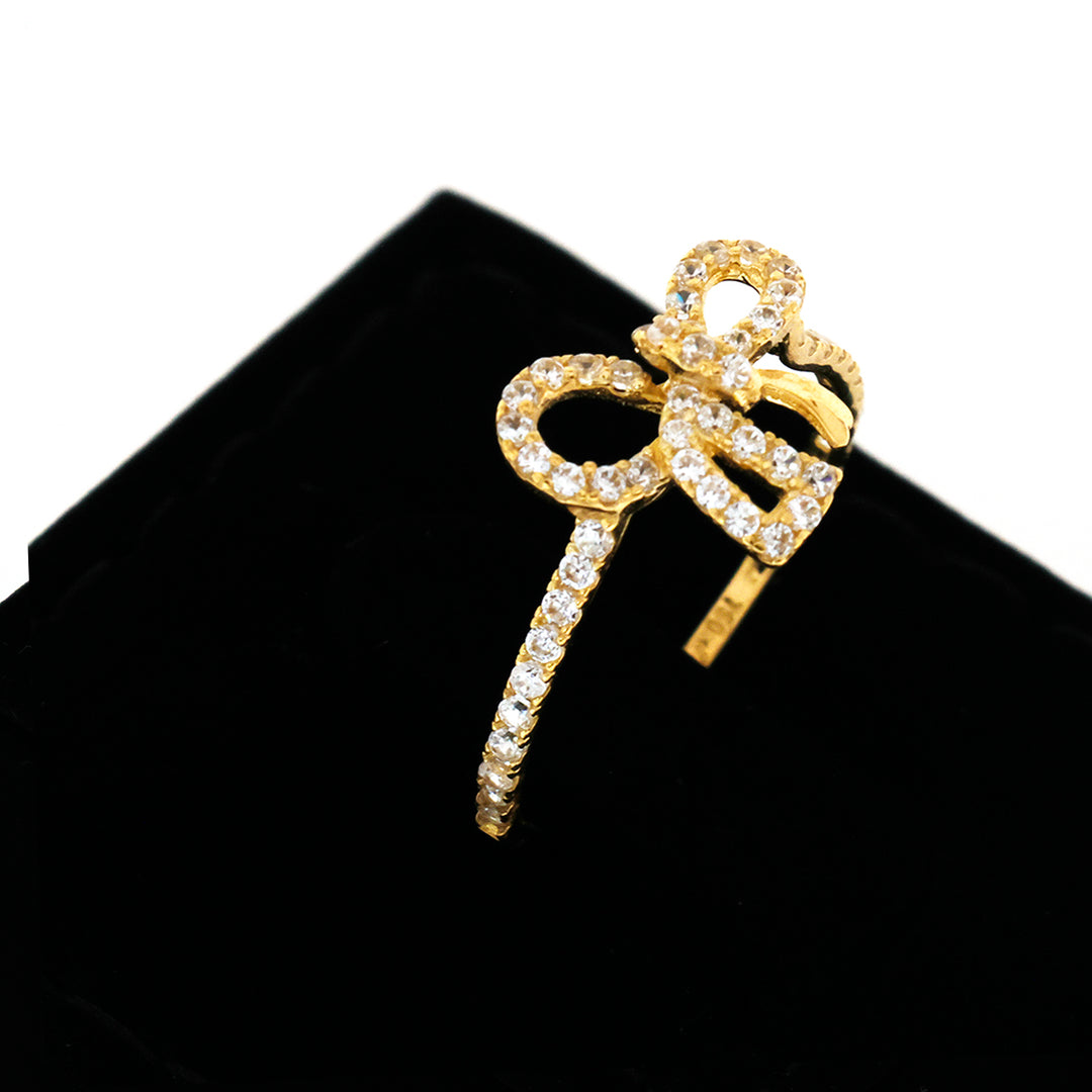 Gold bow-shaped earring with clear stones on a black stand
