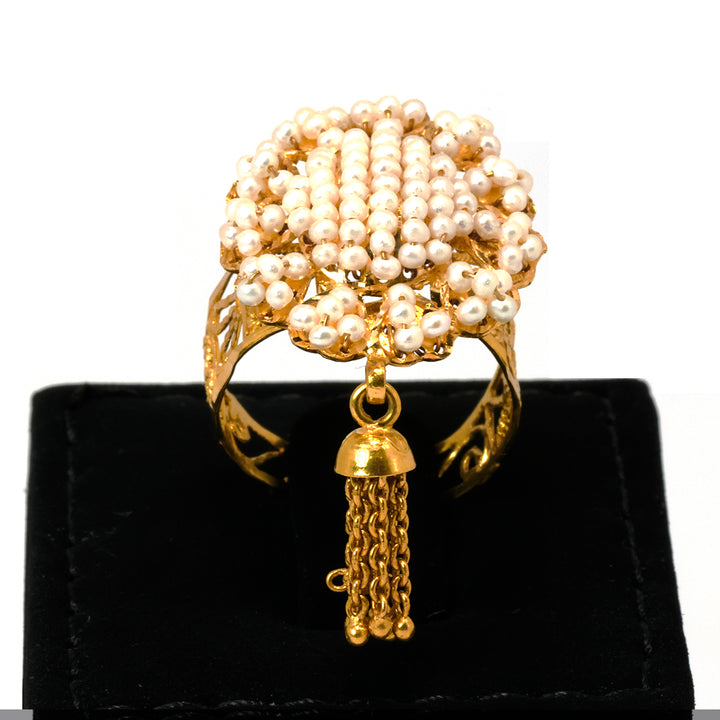 Gold ring with pearl-like beads and a tassel charm on a black stand.