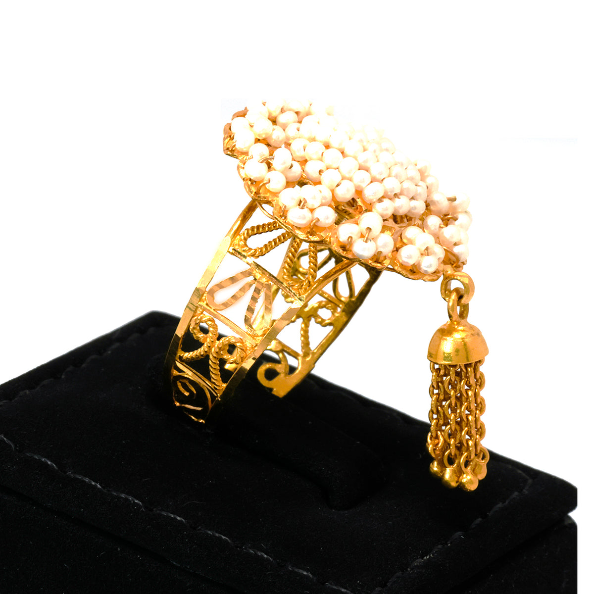 Gold ring with pearls and tassel on a black stand against a white background