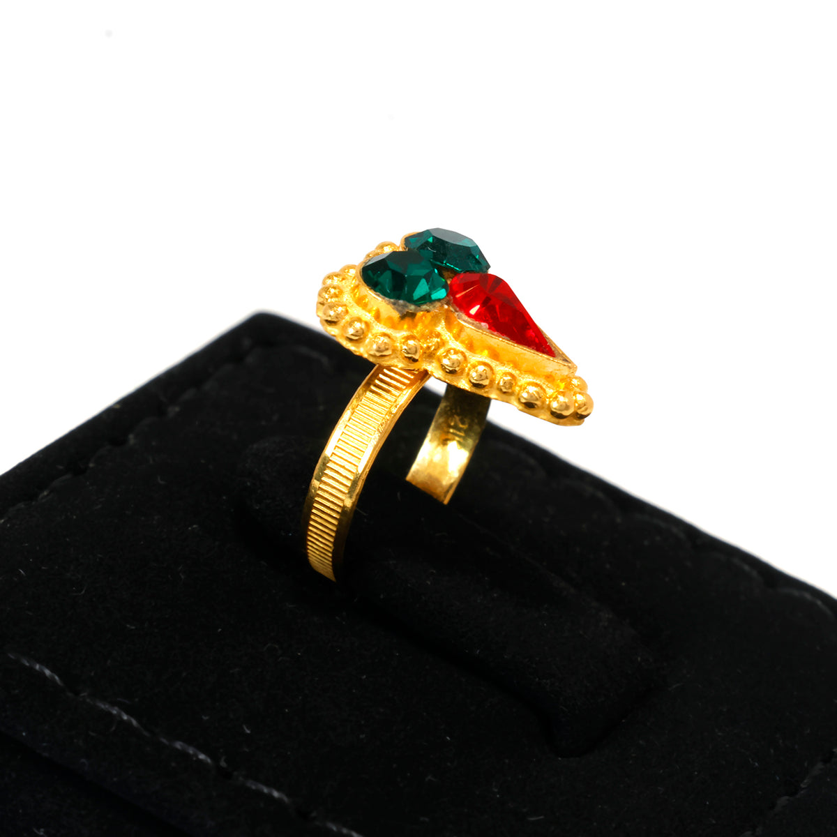 Gold ring with green and red gemstones on a black cushion