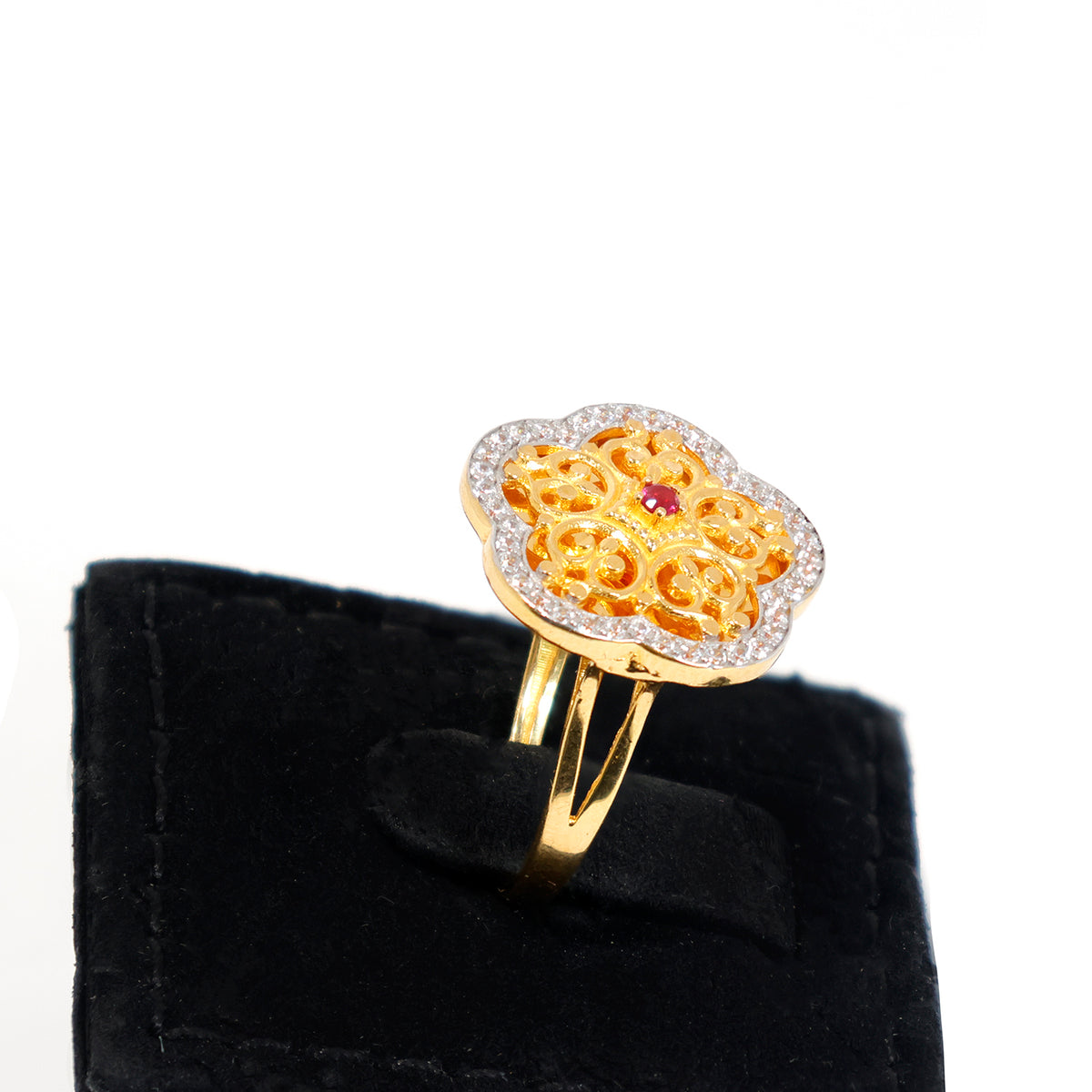 Gold ring with intricate design and red gemstone on a black velvet stand against a white background
