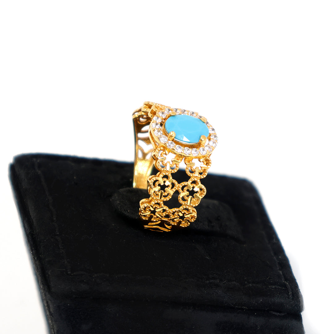 Gold ring with a blue gemstone on a black cushion against a white background