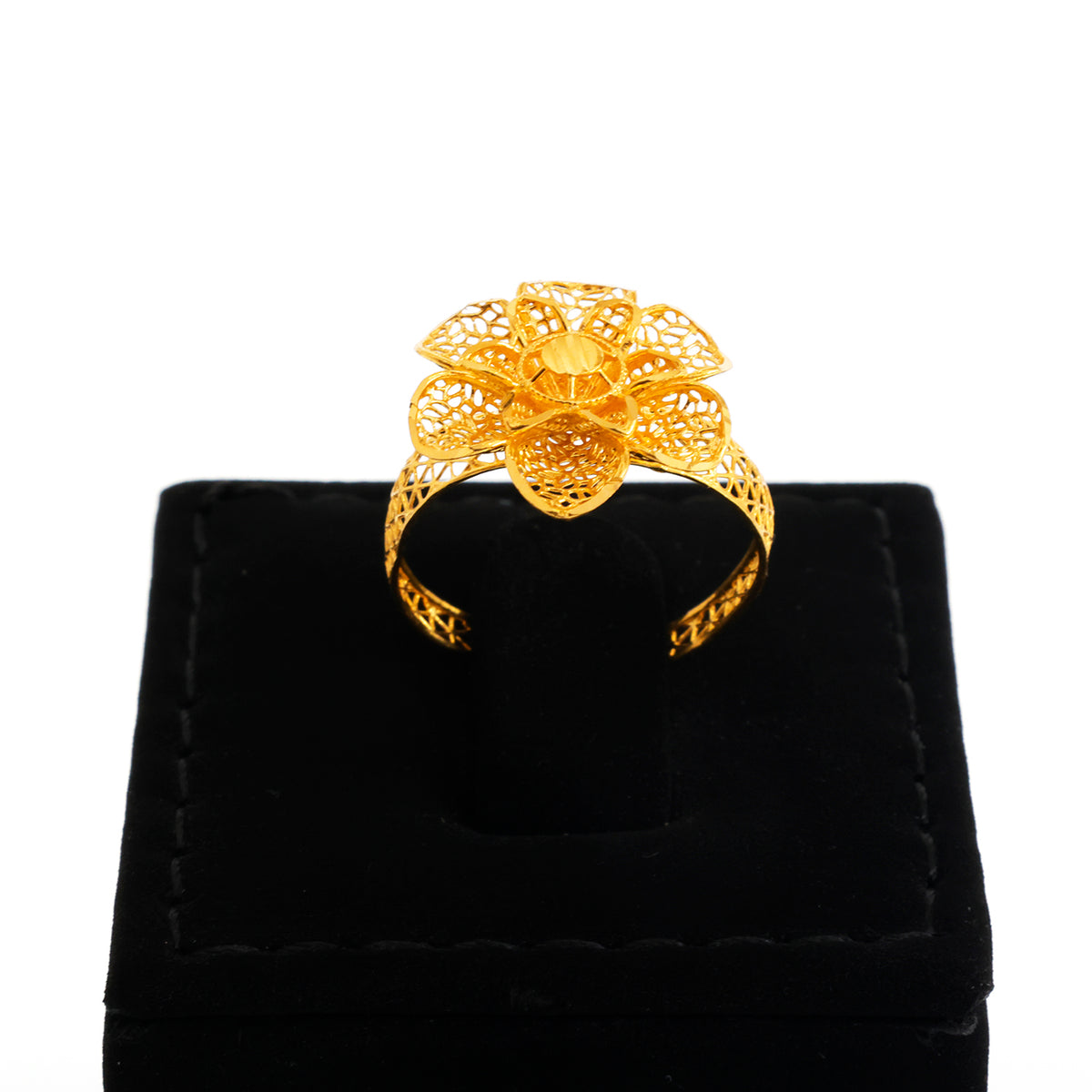 Gold ring with intricate design on a black velvet stand against a white background