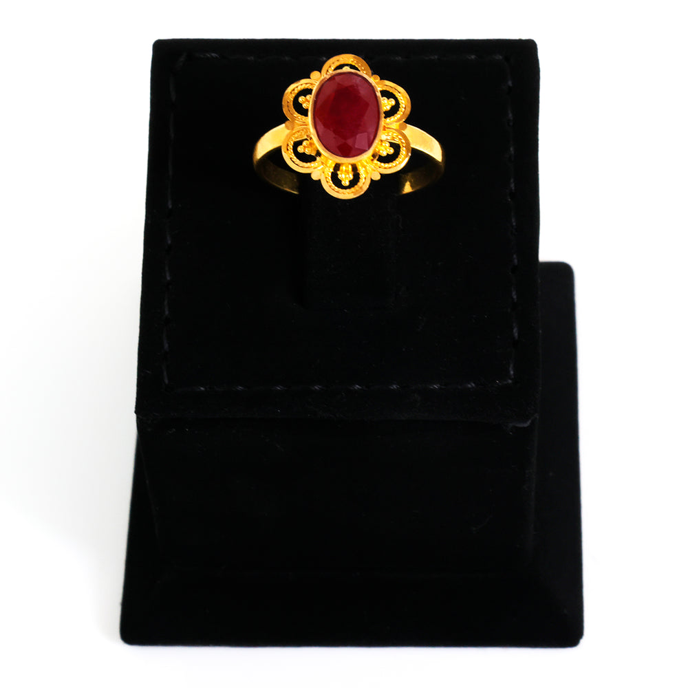 Gold ring with a red gemstone on a black velvet stand
