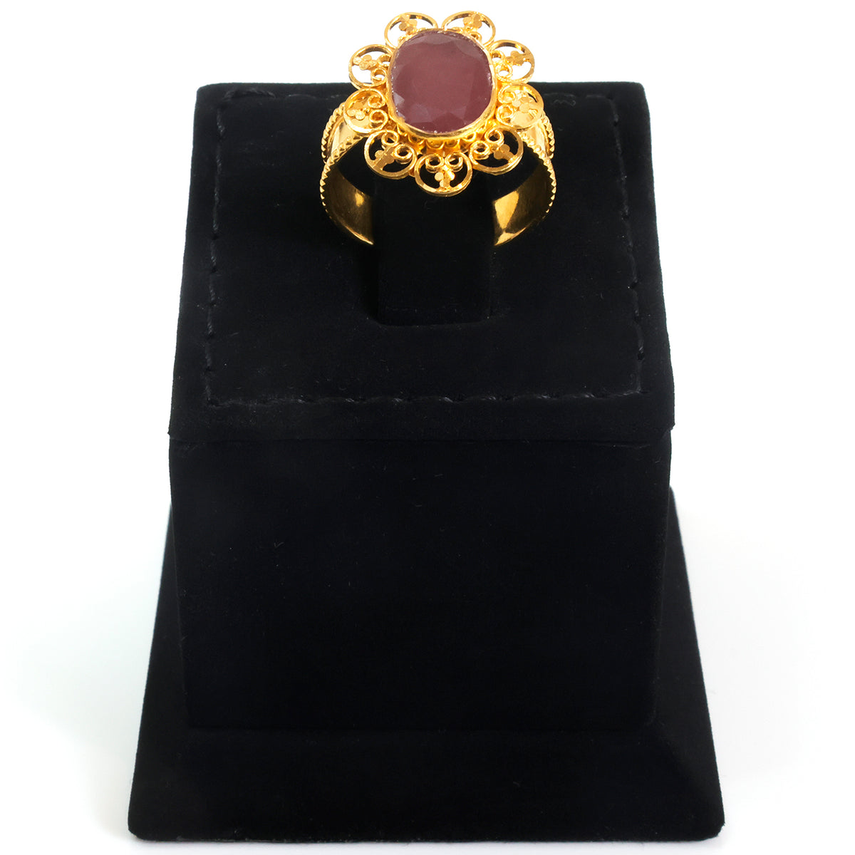 A gold filigree ring with an oval reddish-brown gemstone, displayed on a black velvet ring stand against a white background.