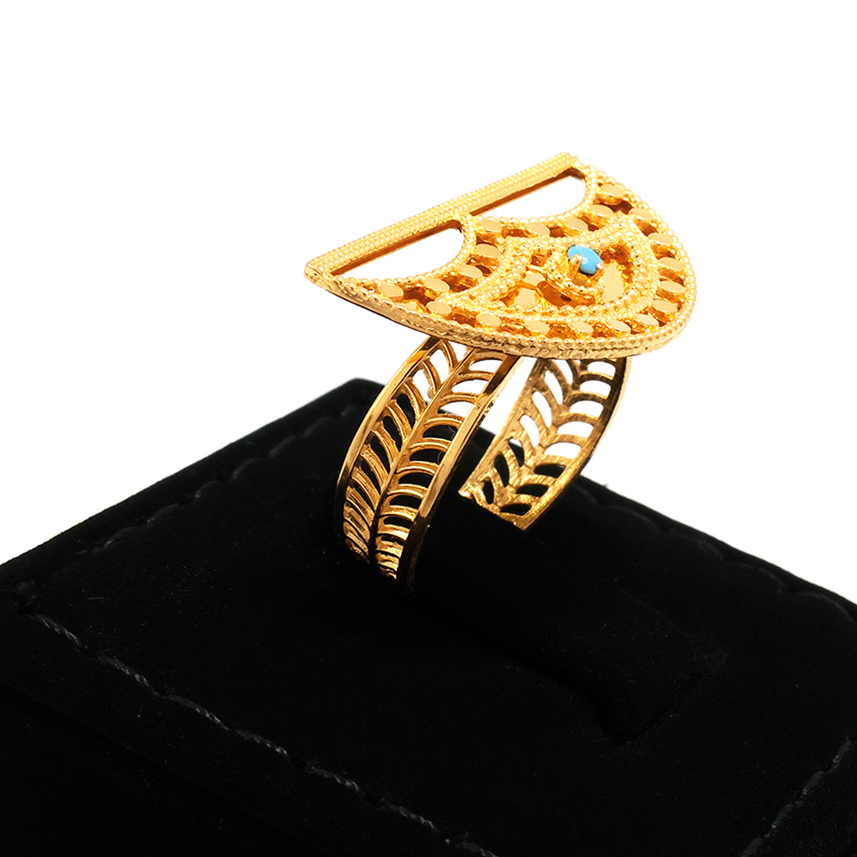 Gold ring with intricate design on a black cushion against a white background