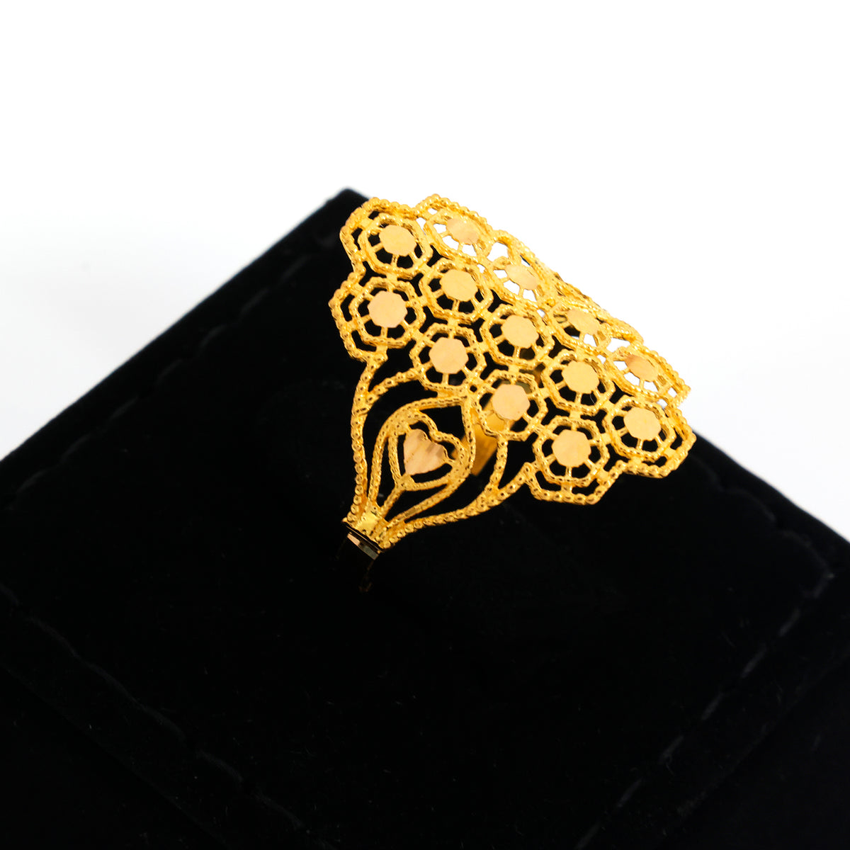 A gold filigree ring with an intricate openwork floral pattern, displayed on a black velvet ring box against a white background.