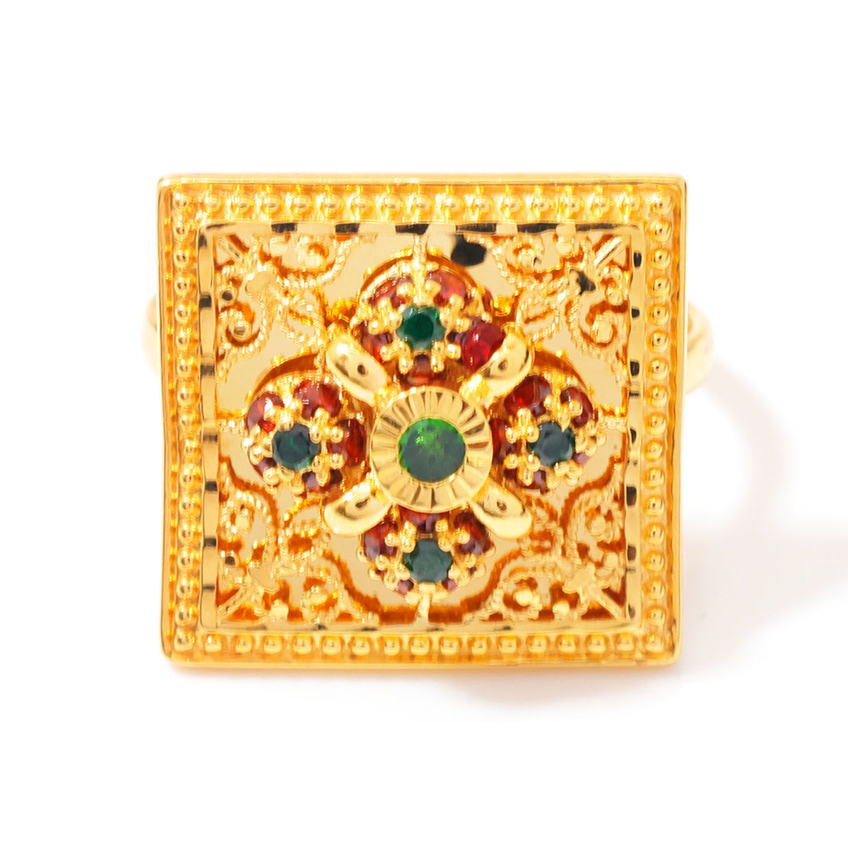 A square gold ring with intricate filigree detailing, featuring a central floral motif with green and red stones, set against a plain white background.