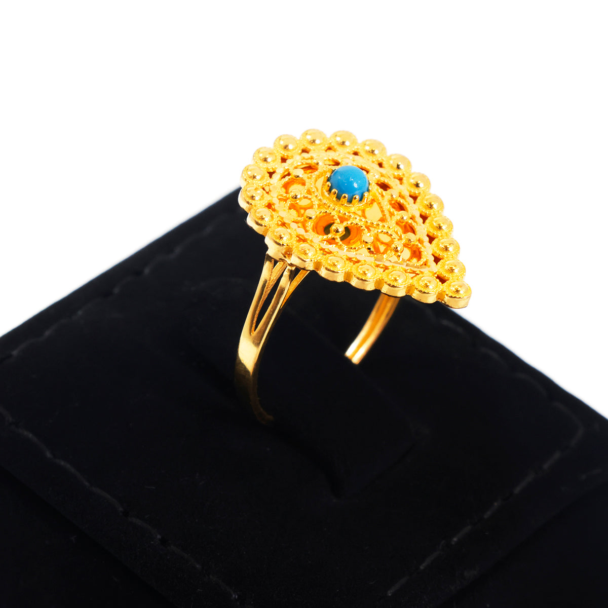A gold ring with an intricate filigree leaf-shaped top and a small blue stone in the center, displayed on a black ring box against a white background.