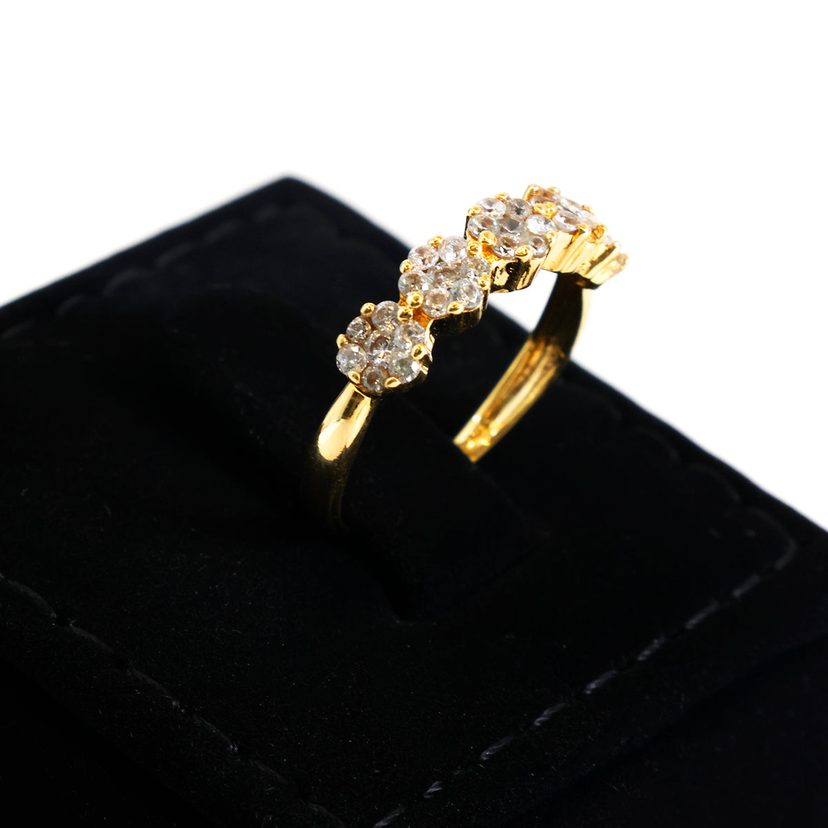 A yellow gold ring with three small round clear gemstones in a row of floral clusters, displayed on a black velvet ring box against a white background.