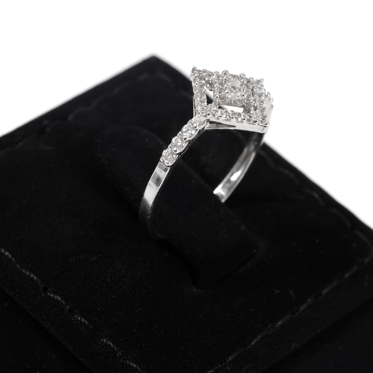 A silver-tone open-shank ring with a large square-cut clear center stone and smaller surrounding stones, displayed on a black velvet ring box against a white background.
