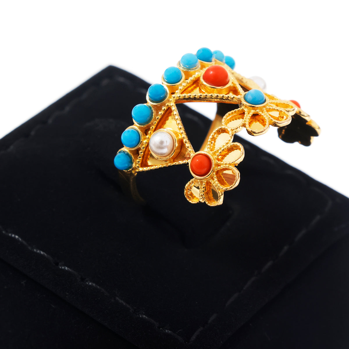 A gold-toned open cuff ring decorated with turquoise blue beads, coral red stones, and a white pearl, displayed on a black velvet ring box.