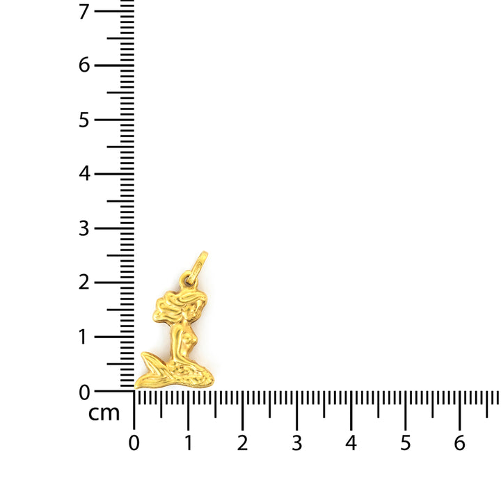 Gold mermaid pendant next to a ruler on a white background