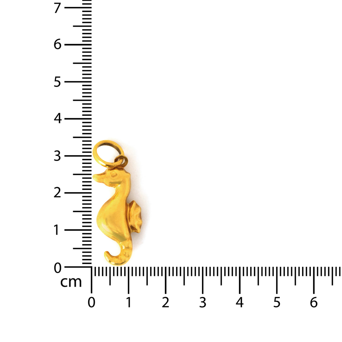 Gold seahorse charm next to a ruler on a white background