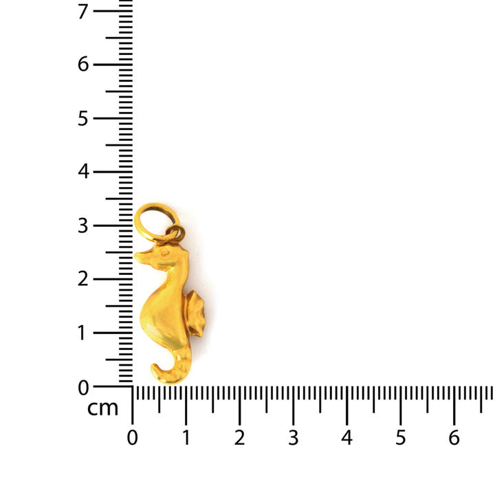 Gold seahorse charm next to a ruler on a white background