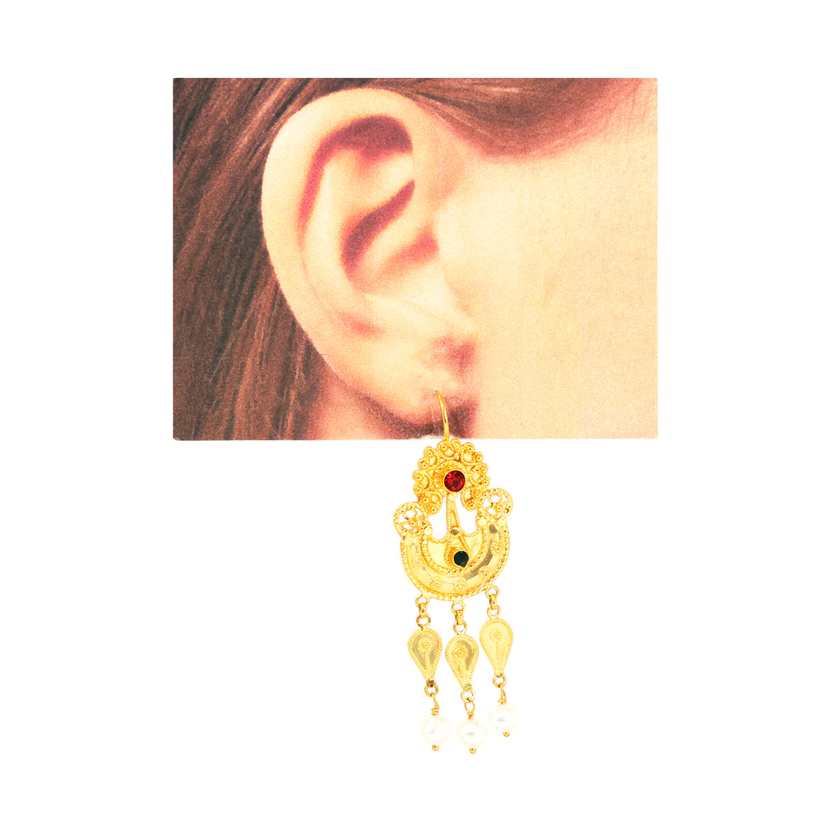 Gold earring with red gemstone worn on an ear against a white background
