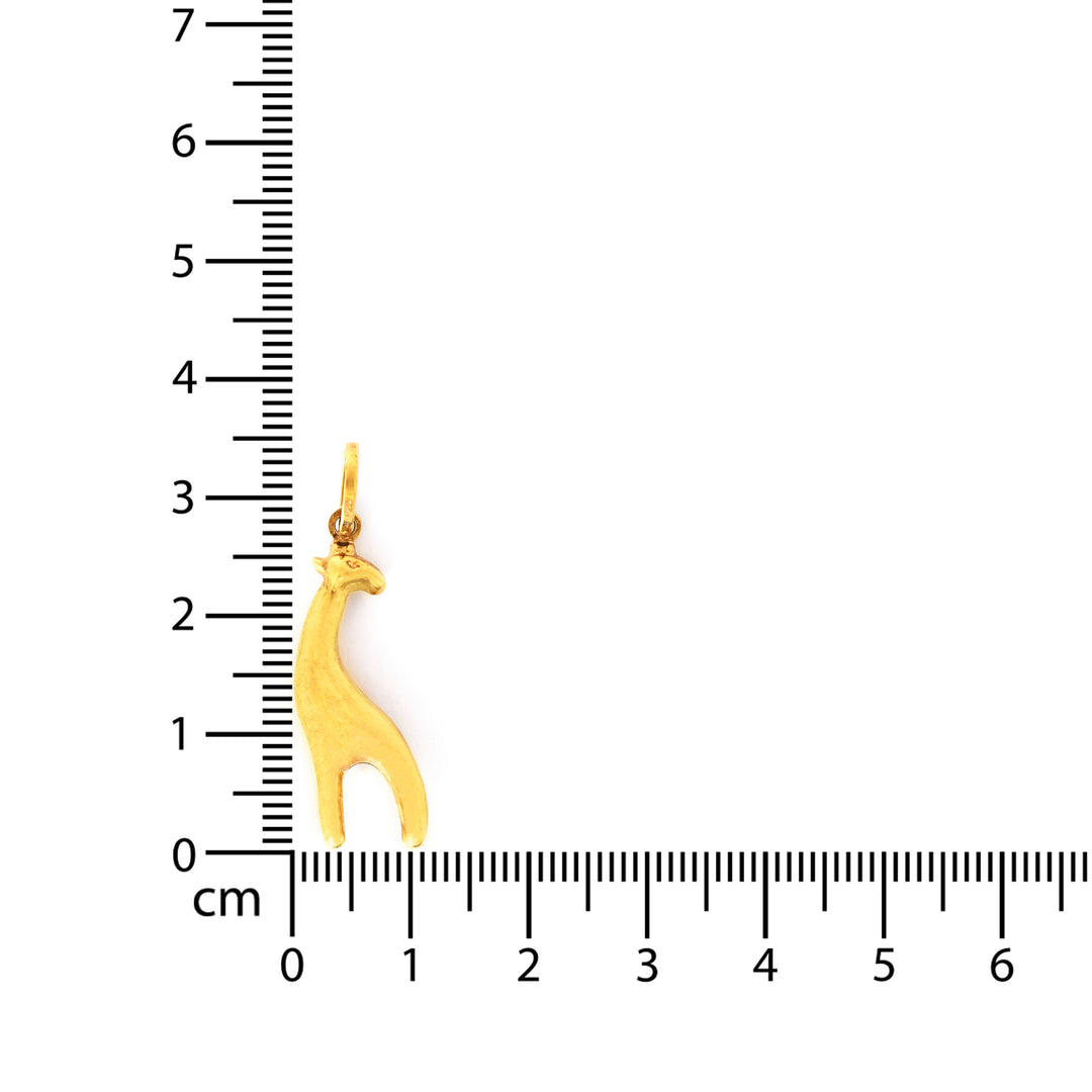 Gold giraffe pendant next to a ruler on a white background