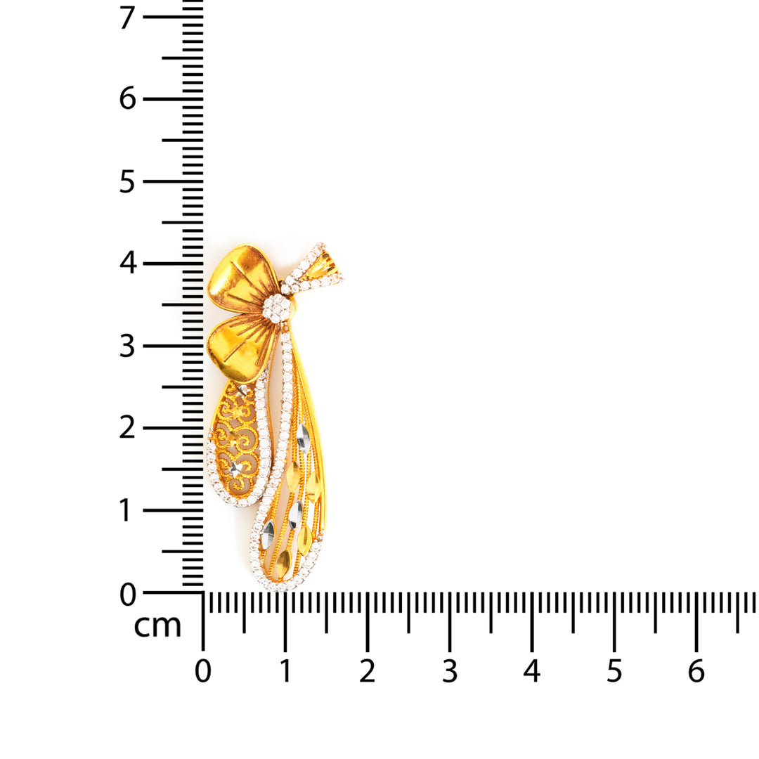 Gold bow-shaped pendant with a ruler for scale on a white background